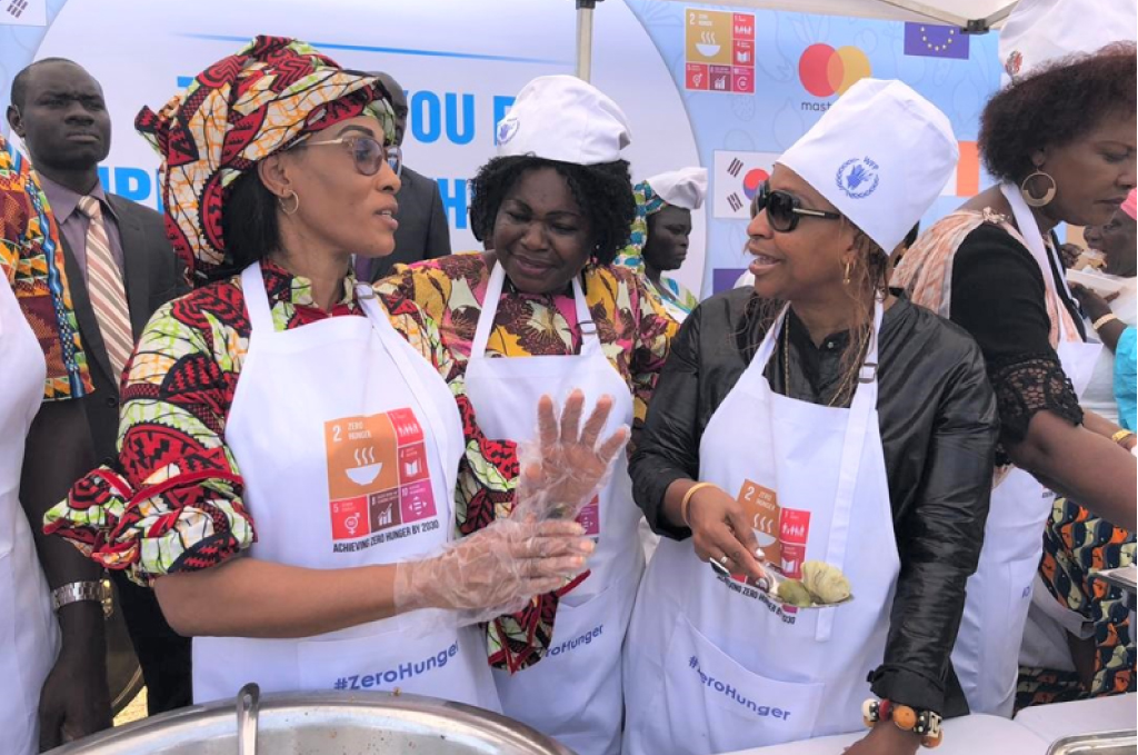 A primeira-dama da Gâmbia, Fattoumatta Bah Barrow, a ministra do Ensino Básico e Secundário, Claudina Cole, e a diretora do WFP na Gâmbia, Wanja Kaaria, servem refeições escolares para os alunos durante as celebrações do Dia Africano da Alimentação Escolar na Gâmbia, em 2018. Foto: WFP/Kebba Jallow.