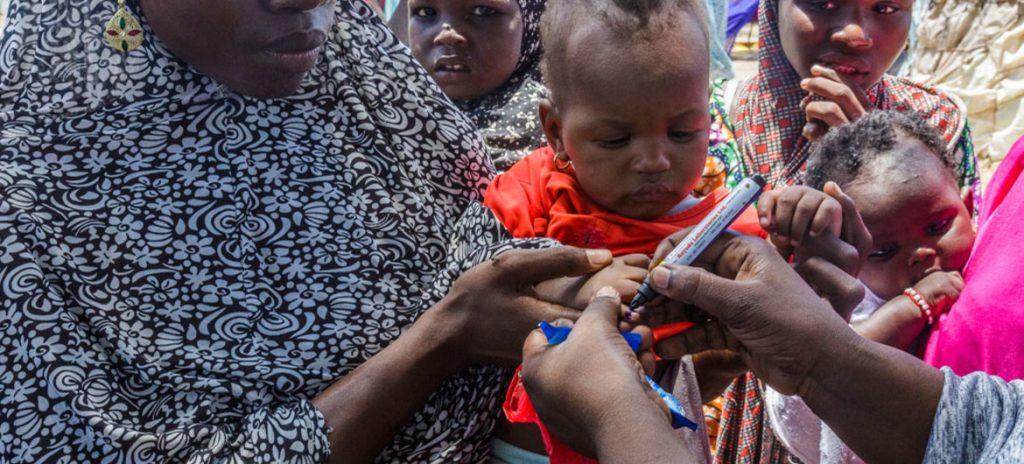 Profissional de saúde do UNICEF usa caneta para marcar o polegar de Ajeda Mallam, de 6 meses, que acaba de ser vacinado contra a poliomielite em um campo para pessoas deslocadas internamente em Maiduguri, no nordeste da Nigéria. Foto: UNICEF / Andrew Esiebo