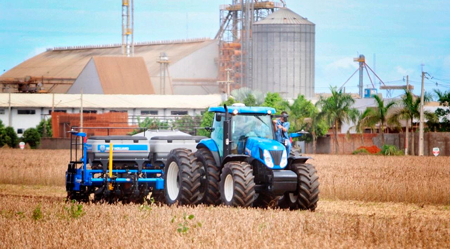 #PraCegoVer Trator na plantação de soja com os silos ao fundo