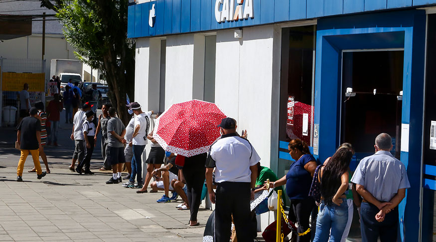 #PraCegoVer Pessoas em fila na porta de uma agênica a Caixa econômica Federal