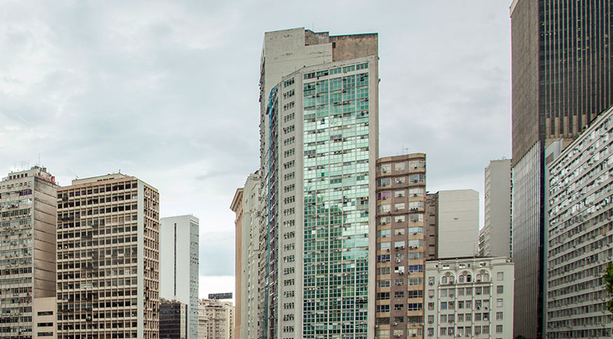 #PraCegoVer Fachada de prédios comerciais com o céu com nuvens brancas