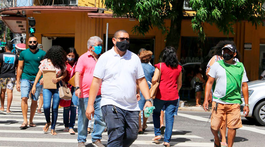 #PraCegoVer Pessoas de máscaras atravessam a rua. Em primeiro plano um homem barrigudo de camisa branca e máscara preta