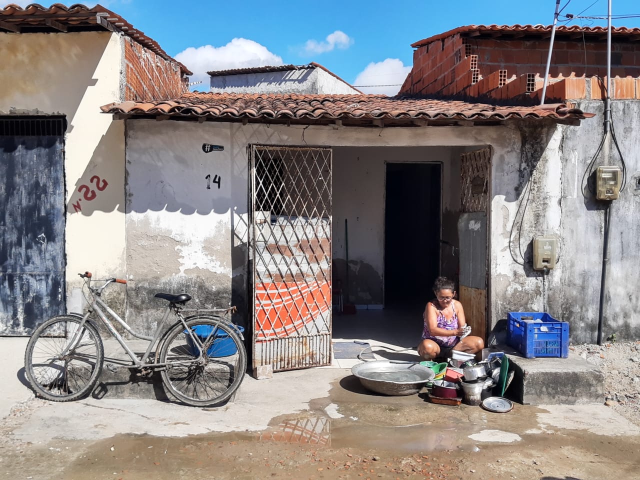 Mulher sentada a frente de casa, lavando a louça na calçada