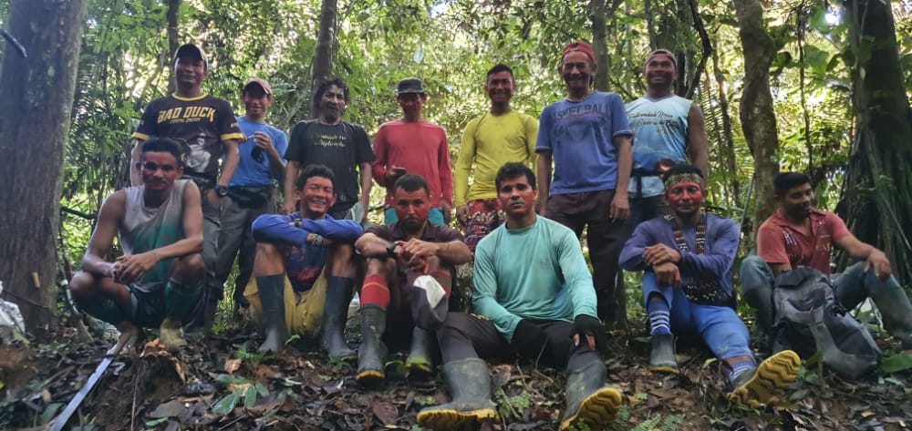 Homens indígenas posam lado a lado em meio à floresta