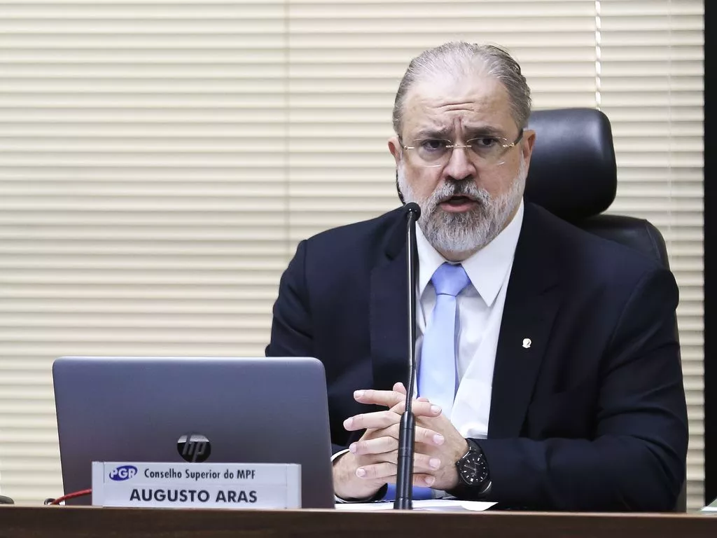 Augusto Aras é um homem branco com cabelo e barba grisalhas. Veste terno preto com gravata azul.