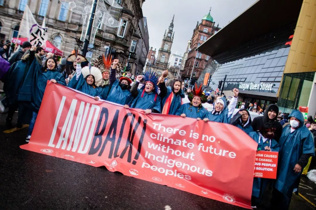 Mulheres indígenas marcham em manifestação na COP-26 com punhos cerrados e em riste, elas seguram um cartaz vermelho que diz "não há futuro climático sem indígenas"