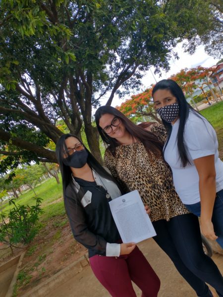 Na foto, três mulheres sorriem e seguram um documento