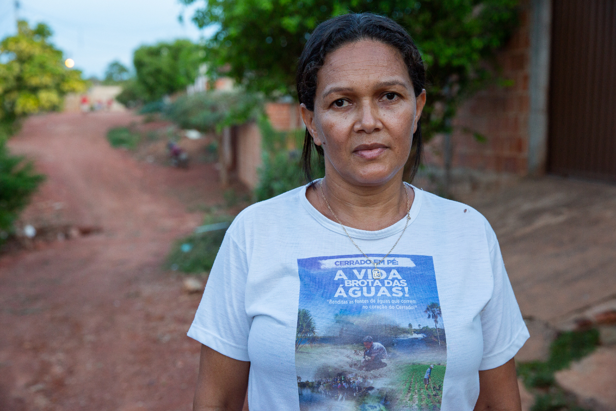 Aline é uma mulher negra com cabelos escuros; ela veste uma camiseta branca com os dizeres "a vida brota da água"