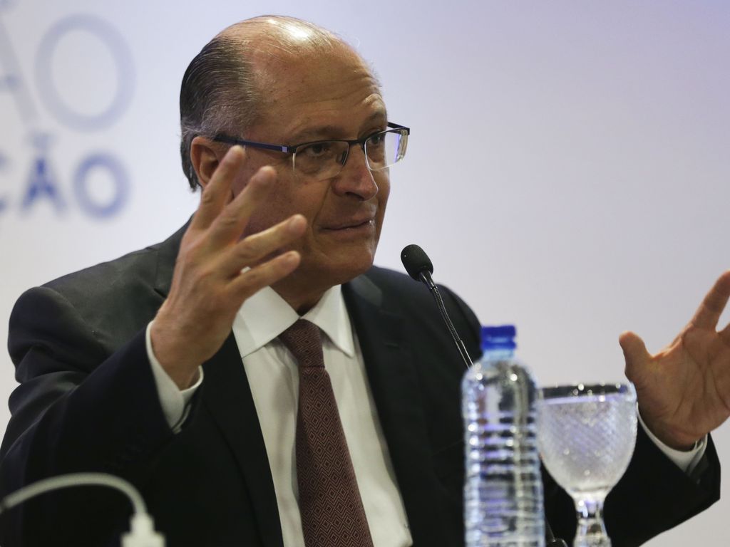 Geraldo Alckmin é um homem branco na faixa dos 50 anos, calvo e com cabelos grisalhos; ele veste um terno preto e óculos de grau