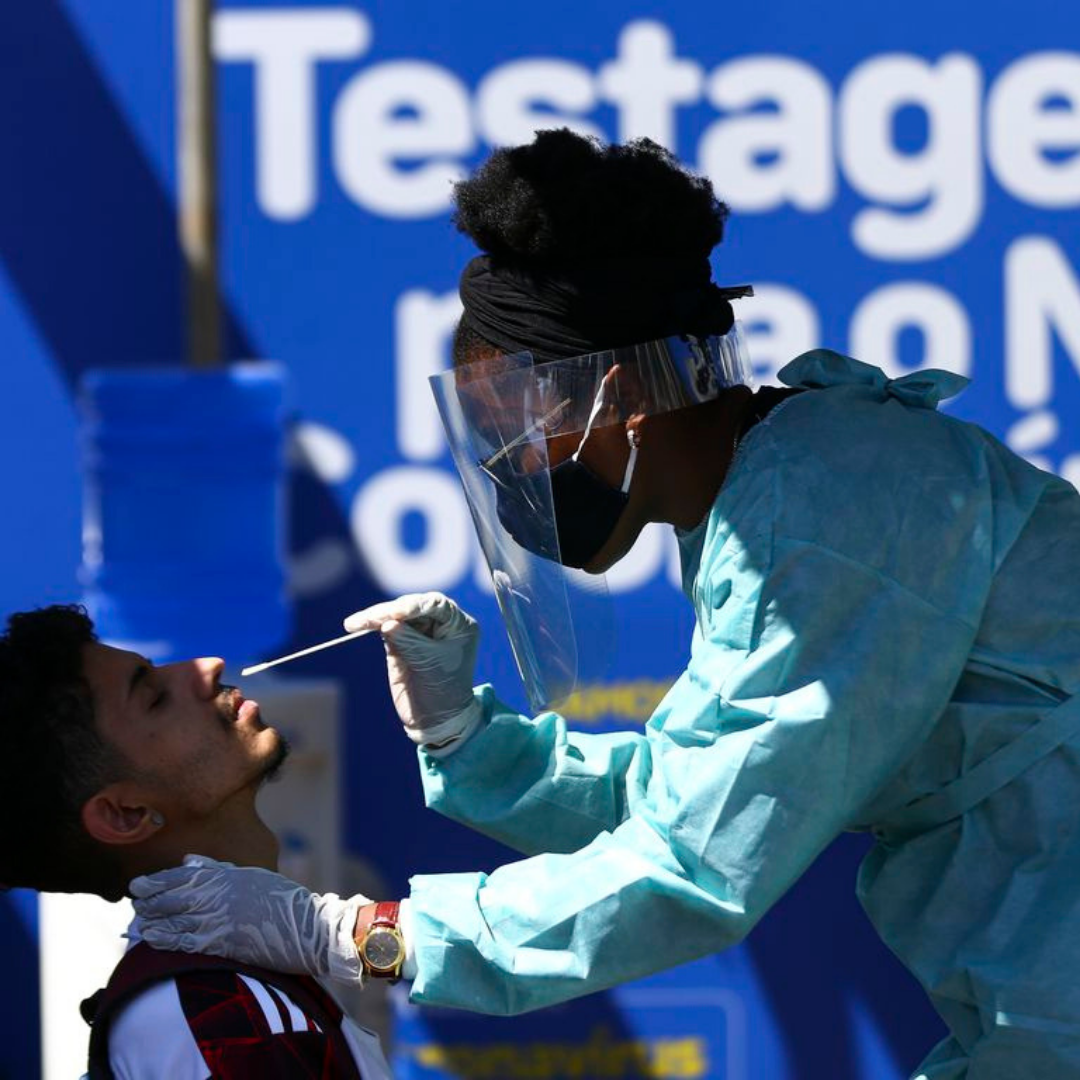 Enfermeira de jaleco azul realiza teste de covid-19 em adolescente