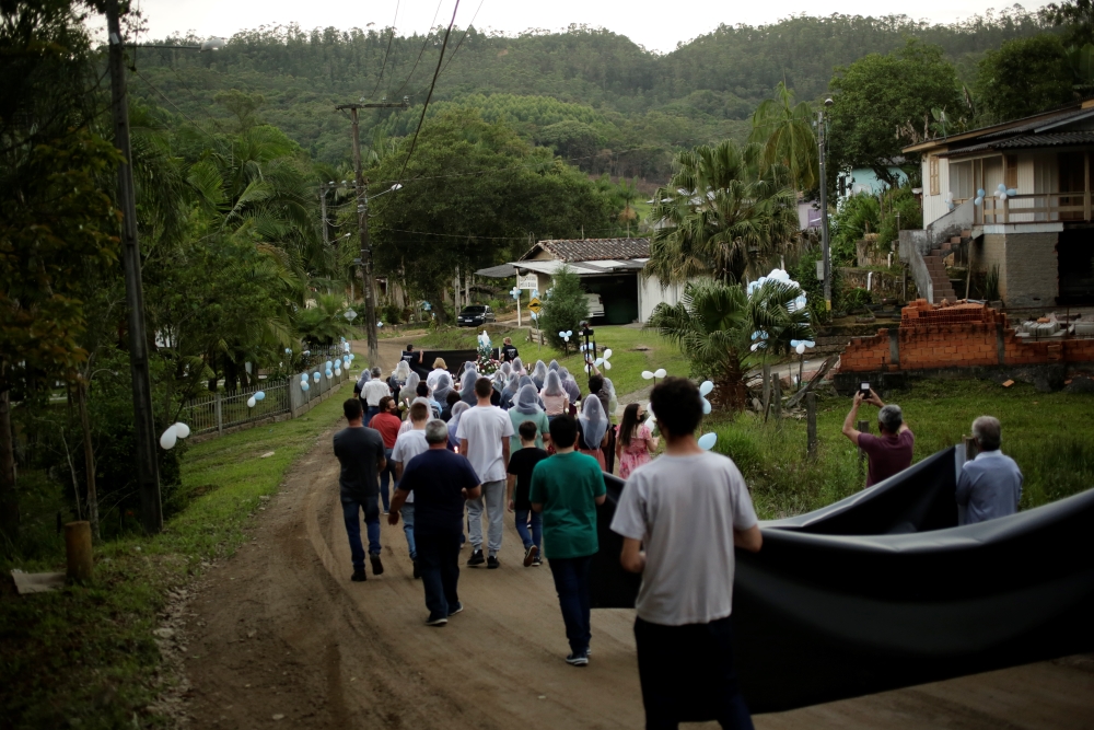 Procissão pelas vítimas de carvão se estende por ruas de uma zona rural, com dezenas de pessoas andando com velas nas mãos