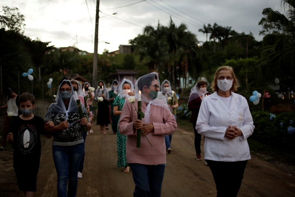 A imagem mostra dezenas de pessoas caminhando em uma procissão com velas nas mãos