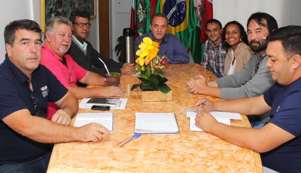 Oito pessoas, entre homens e mulheres, estão sentadas à mesa; todos olham para a câmera