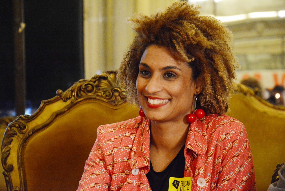 Marielle Franco era uma mulher negra, com cabelo agro curto e castanho; ela vestia uma blusa florida vermelha