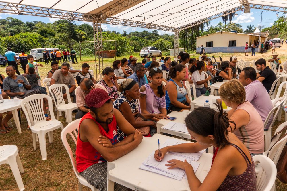 Atingidos e atingidas pela tragédia de Brumadinho buscam ajuda; na imagem é possível ver pessoas sentadas em mesa preenchendo formulários