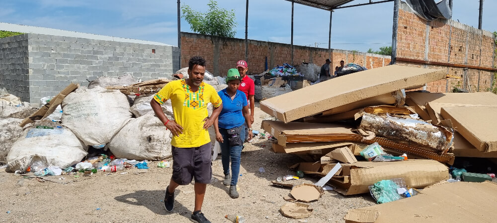 Tião é um homem negro, ele veste uma camiseta amarela e caminha entre o lixo com funcionários da sua cooperativa