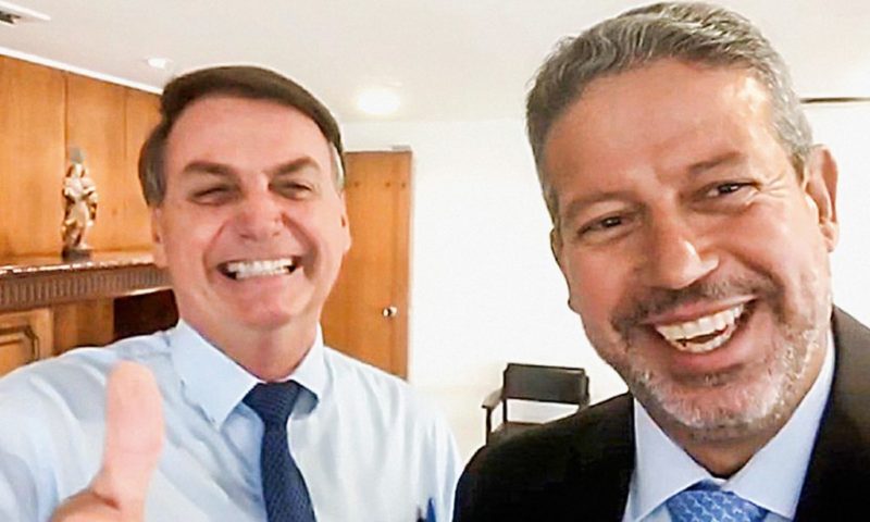 Jair Bolsonaro (à esquerda) é um homem branco na faixa dos 60 anos, ele veste camisa azul claro e gravata azul escuro; Já Arthur Lira (à direita) é um homem branco com cabelos grisalhos, olhos castanhos, ele veste terno preto com gravata azul