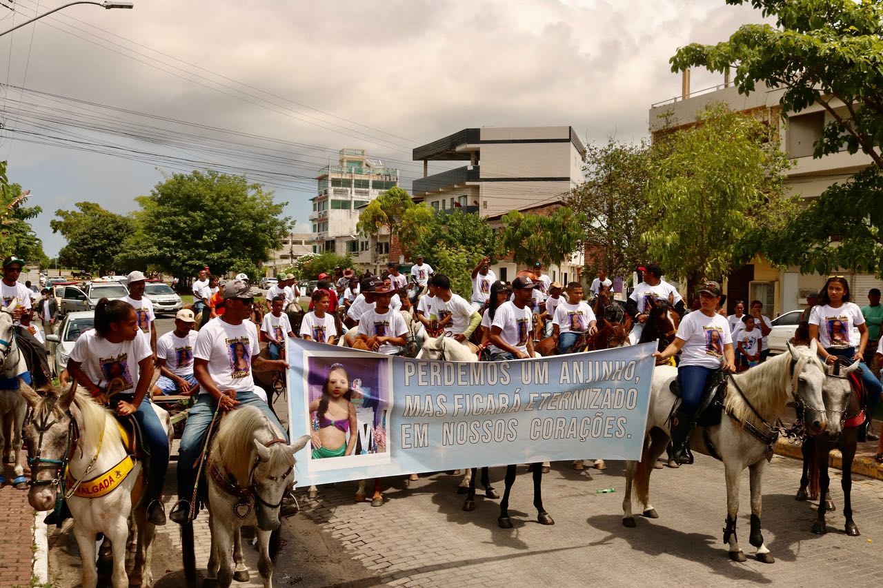 Moradores andam a cavalo em ruas de comunidade em Porto de Galinhas, e seguram uma faixa com a foto de Heloysa, criança assassinada pela polícia