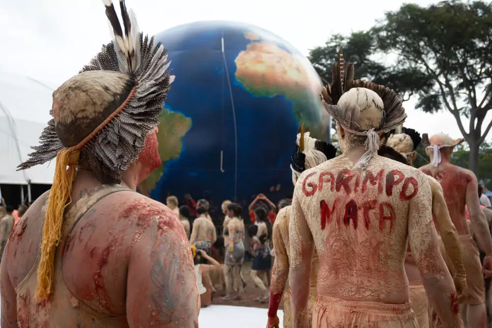 Na foto é possível ver homens e mulheres indígenas com seus corpos sujos de lama, a maioria usa cocar na cabeça. Um deles, em destaque na foto, tem a frase "garimpo mata" escrito de vermelho nas costas. Ao fundo do grupo está um balão azul imitando o formato do planeta terra