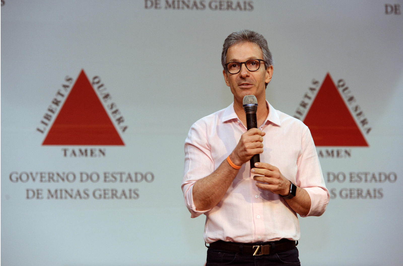 Romeu Zema é um homem branco com olhos castanhos e cabelos grisalhos, ele veste uma camisa social rosa bebê