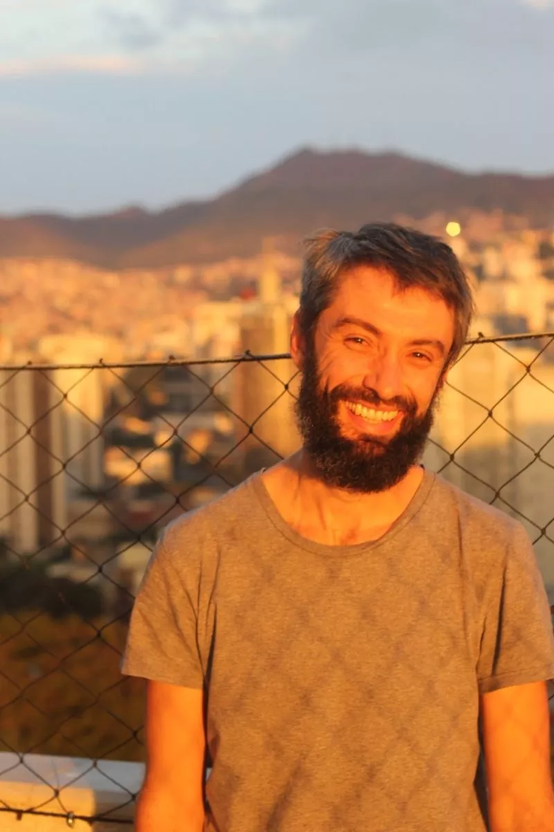 Roberto Andrés é um homem branco com cabelos e barba castanhos; ele veste uma camiseta cinza. Ao fundo está a Serra do Curral