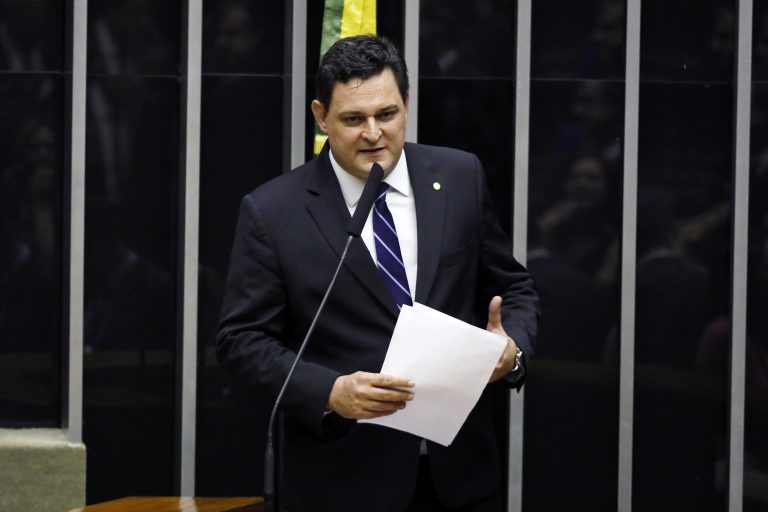 Deputado Geninho Zuliani discursa no Plenário da Câmara. Ele é branco, tem o cabelo escuro, usa um terno preto e segura um papel