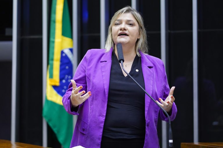 Deputada Professora Luciene Cavalcante fala ao microfone. Ela é branca, tem o cabelo longo e loiro, usa um blazer lilás