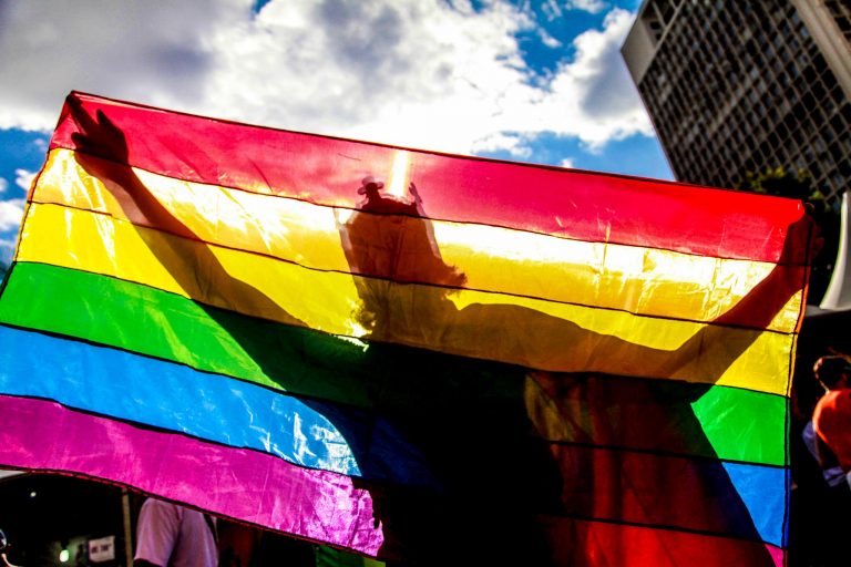 Pessoa segura uma bandeira com as cores do arco-íris