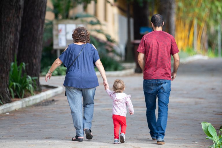 Pai, mãe e filha caminham por uma rua