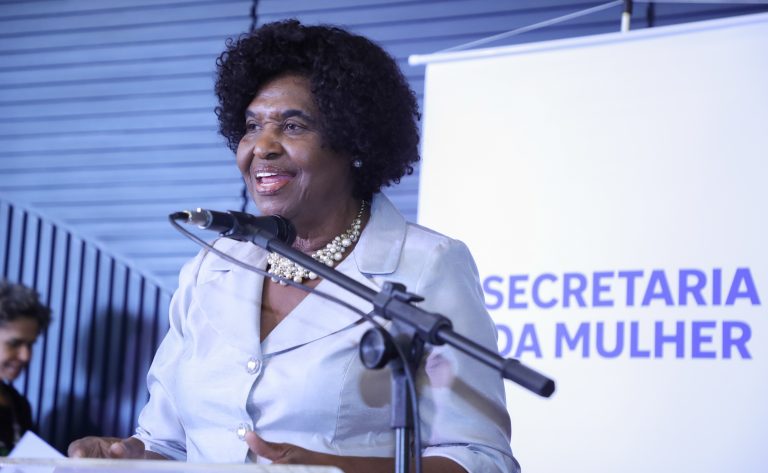 Deputada Benedita da Silva fala ao microfone. Ela é negra, tem cabelo curto e usa um blusa bege