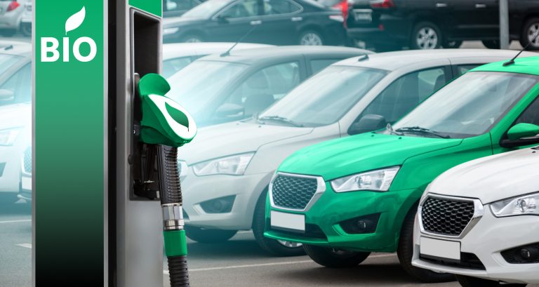 Uma bomba de combustível verde. Ao fundo alguns carros parados