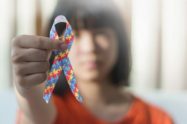 Uma menina desfocada segura uma fita com o símbolo do autismo