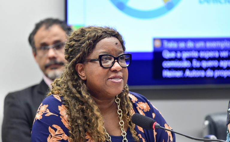 A ministra Macaé Evaristo fala ao microfone. Ela é uma mulher negra, tem o cabelo crespo e usa óculos
